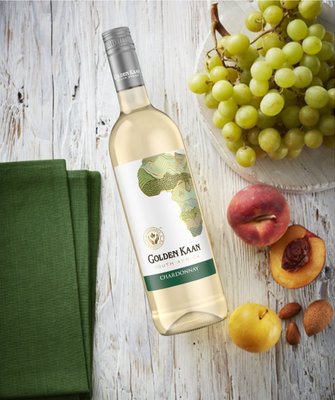 Auf einem Holzuntergrund liegt eine Flasche Golden Kaan Chardonnay, umgeben von saftigen Trauben und frischem Obst.