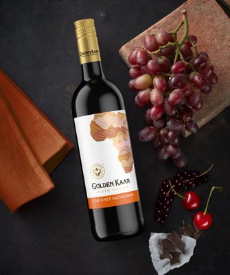 Eine Flasche Golden Kaan Cabernet Sauvignon steht neben frischen Trauben und Kirschen auf einem dunklen Untergrund.
