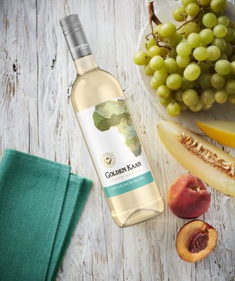 Eine Flasche Golden Kaan Sauvignon Blanc liegt auf einem Holztisch, umgeben von frischen Trauben und geschnittenem Obst.