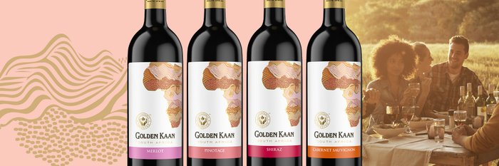 Vier Flaschen Golden Kaan Wein stehen vor einer fröhlichen Gruppe von Freunden, die im Freien zusammen essen und trinken.