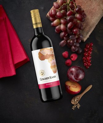 Auf dem Tisch liegt eine Flasche Golden Kaan Shiraz, umgeben von frischen Früchten wie Trauben, Himbeeren und einer Pflaume.