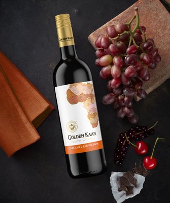 Eine Flasche Golden Kaan Cabernet Sauvignon steht neben frischen Trauben und Kirschen auf einem dunklen Untergrund.