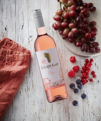 Auf einem Holzuntergrund liegt eine Flasche Golden Kaan Rosé, umgeben von saftigen Trauben und frischem Obst.